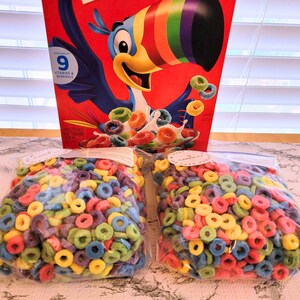 May include: A box of colorful cereal with a toucan mascot and bags of the same cereal. The cereal pieces are ring-shaped and come in various colors, including red, yellow, green, and blue. The box has the text "9 Vitamins & Minerals".