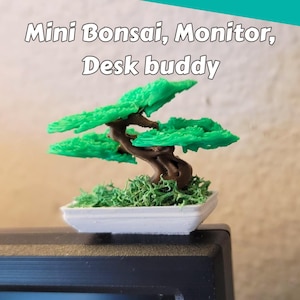May include: A miniature bonsai tree figurine with a brown trunk and bright green foliage, set in a small white rectangular pot with green moss-like texture. The text "Mini Bonsai, Monitor, Desk buddy" is displayed above the object.