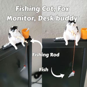 May include: A black and white cat figurine sitting on a black monitor mount, holding a thin fishing rod with a small fish attached to the line. An orange bucket sits next to the cat. The text Fishing Cat, Fox Monitor, Desk buddy is visible.