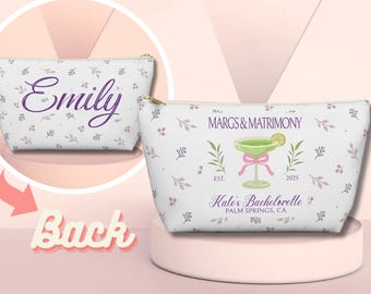 May include: White cosmetic bag with a floral pattern and gold zipper. The bag features the text "Emily" in purple script on the front. The other bag has a margarita graphic and text "MARGS & MATRIMONY" and "Kate's Bachelorette" on the front.