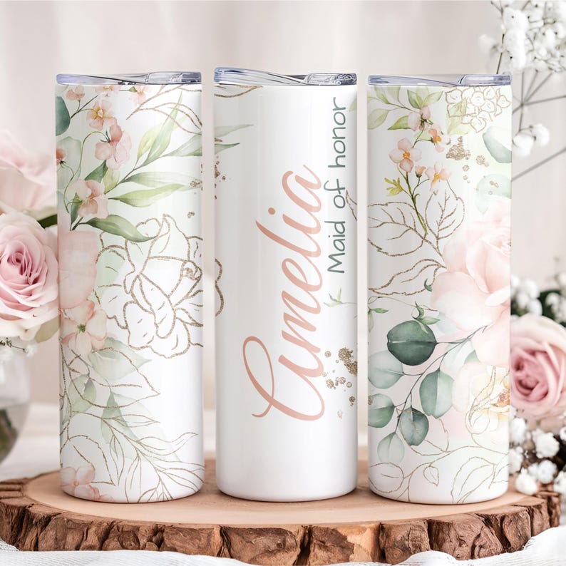 May include: Three white stainless steel tumblers with floral designs and lids. One tumbler has the name "Amelia" and the text "Maid of honor" in rose gold script. The other two tumblers feature pink and green floral patterns.