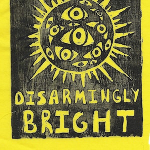 May include: A black and yellow print with the words "THE FUTURE'S DISARMINGLY BRIGHT." The design features a sun with many eyes. The background is bright yellow.