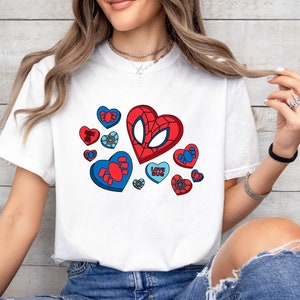 May include: White t-shirt with a red and blue graphic of a Spiderman mask inside a heart.  The graphic is surrounded by smaller hearts with spiderwebs and the text "Love Bug".
