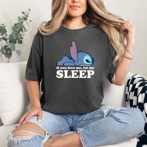 Puede incluir: Una camiseta gris oscuro con un personaje de dibujos animados azul Stitch acostado y el texto "Si me quieres, d&eacute;jame DORMIR".