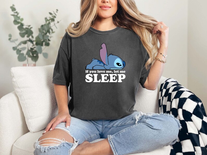 Puede incluir: Una camiseta gris oscuro con un personaje de dibujos animados azul Stitch acostado y el texto "Si me quieres, d&eacute;jame DORMIR".