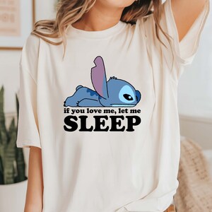 Puede incluir: Una camiseta blanca con un personaje de dibujos animados azul acostado y el texto "if you love me, let me SLEEP".