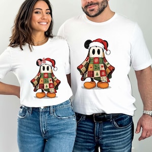 May include: White t-shirts with a cartoon ghost character in a Christmas Santa hat and patchwork quilt costume. The ghost has Mickey Mouse ears and orange shoes. The woman's shirt has a red bow. Both wear blue jeans.