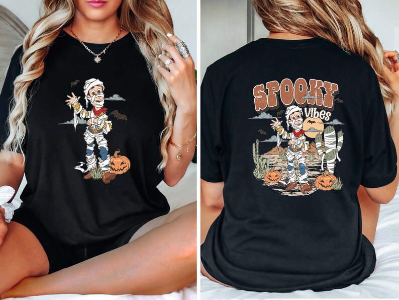 Puede incluir: Camiseta negra con un gr&aacute;fico de momia de dibujos animados y el texto "Spooky Vibes" impreso en la espalda.