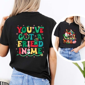 Peut inclure: T-shirt noir avec un motif color&eacute; qui dit "You've Got A Friend In Me" avec un bonhomme de neige et des lumi&egrave;res de No&euml;l. Le t-shirt est port&eacute; par une personne.