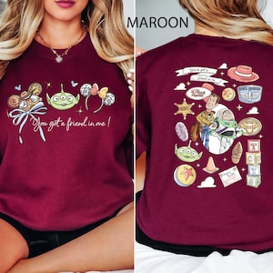 May include: Maroon sweatshirt featuring a colorful graphic of Disney characters and the phrase "You got a friend in me!" on the front. The back of the sweatshirt has additional character illustrations. A fun, casual top for Disney fans.
