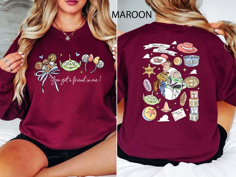 May include: Maroon sweatshirt featuring a colorful graphic of Disney characters and the phrase "You got a friend in me!" on the front. The back of the sweatshirt has additional character illustrations. A fun, casual top for Disney fans.