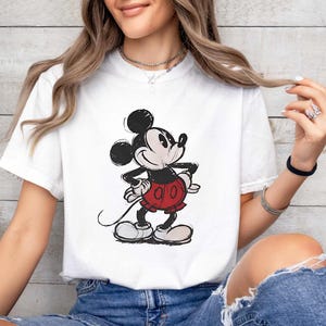 May include: White t-shirt featuring a classic Mickey Mouse graphic. The cartoon character is depicted in black, red, and white, with a vintage, sketched style. The shirt is a casual, short-sleeved design.