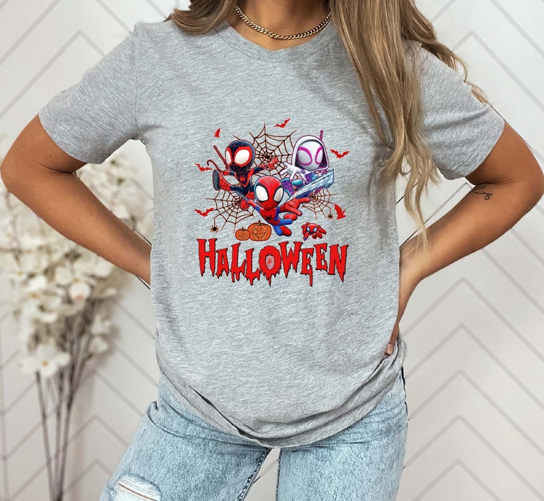 Peut inclure: Un t-shirt gris avec un motif de trois personnages Spider-Man dans une toile d'araign&eacute;e avec des citrouilles et le texte "Happy Halloween".