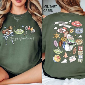 May include: Military green sweatshirt featuring a colorful graphic from the movie Toy Story. The front design includes characters and the phrase "You got a friend in me!". The back displays additional character illustrations and text.