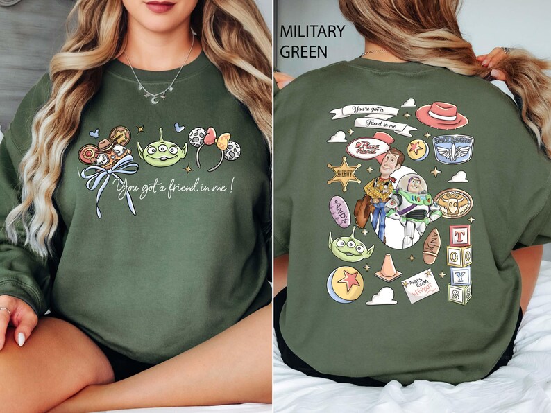May include: Military green sweatshirt featuring a colorful graphic from the movie Toy Story. The front design includes characters and the phrase "You got a friend in me!". The back displays additional character illustrations and text.