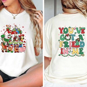 Peut inclure: T-shirt blanc avec un motif d'arbre de No&euml;l repr&eacute;sentant des personnages de la franchise de films Toy Story. Le dos du t-shirt porte le texte "You've got a friend in me" en lettres color&eacute;es.
