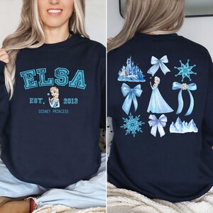 Elsa two sided bow sweatshirt and hoodie inspired by Frozen Disney princess style. Cozy unisex crewneck sweatshirt featuring front and back bow design aesthetic. Perfect Disney girls trip sweatshirt for Disneyland and Disney World vacations. Soft and comfortable Disney sweatshirt ideal for park outfits, travel days, or casual wear. Cute coquette Elsa sweatshirt great for girls, friends, and Disney fans.
