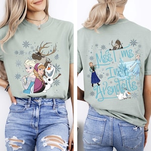 May include: Sage green t-shirt featuring characters from the movie Frozen, including Elsa, Anna, Olaf, and Sven, with snowflake accents. The back of the shirt has the text "Meet me in Arendelle" with additional characters.