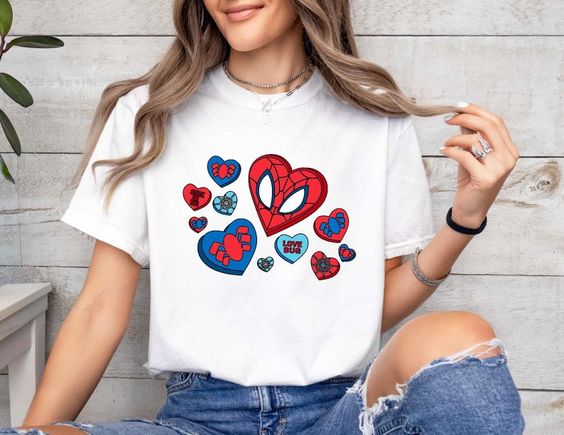May include: White t-shirt with a red and blue graphic of a Spiderman mask inside a heart.  The graphic is surrounded by smaller hearts with spiderwebs and the text "Love Bug".