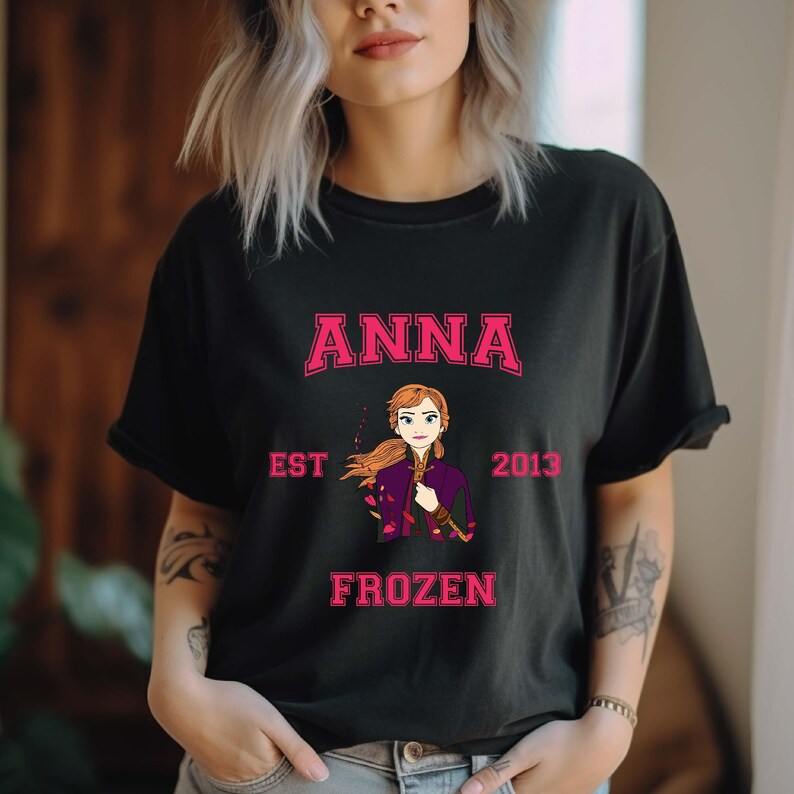 Puede incluir: Camiseta negra con un gr&aacute;fico rosa de Anna de Frozen. El gr&aacute;fico incluye el texto "ANNA", "EST 2013" y "FROZEN".