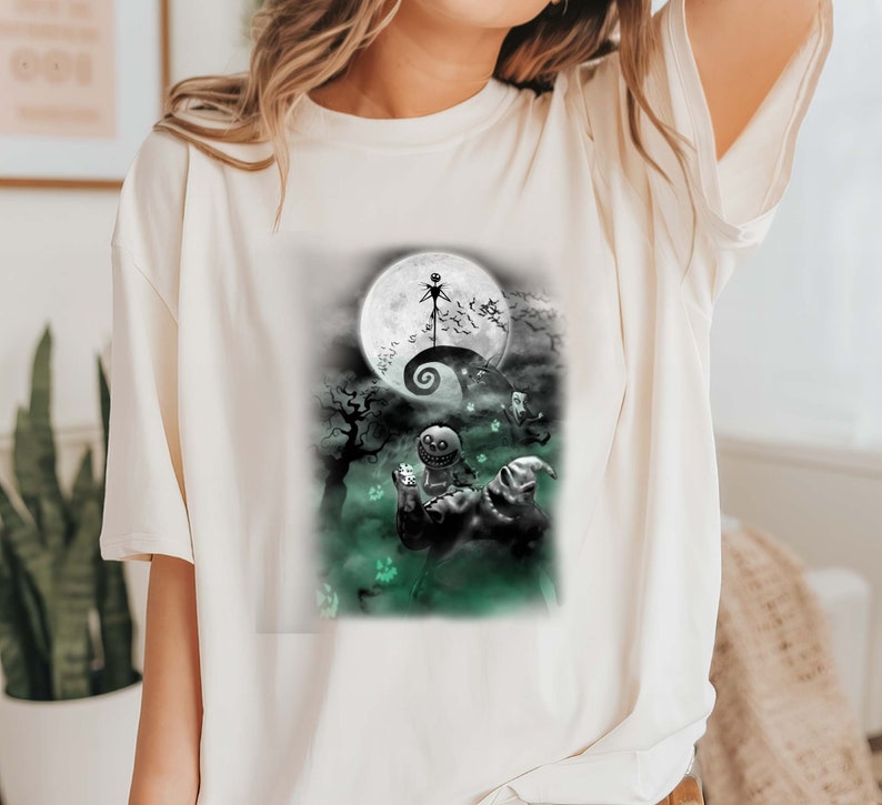 K&ouml;nnte beinhalten: Wei&szlig;es T-Shirt mit einem schwarz-wei&szlig;en Grafikdruck von Figuren aus dem Film Nightmare Before Christmas. Die Grafik zeigt Jack Skellington, Sally und Oogie Boogie vor einem Vollmond.