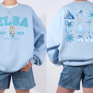 Elsa two sided bow sweatshirt and hoodie inspired by Frozen Disney princess style. Cozy unisex crewneck sweatshirt featuring front and back bow design aesthetic. Perfect Disney girls trip sweatshirt for Disneyland and Disney World vacations. Soft and comfortable Disney sweatshirt ideal for park outfits, travel days, or casual wear. Cute coquette Elsa sweatshirt great for girls, friends, and Disney fans.