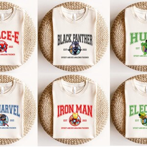 May include: Six cream-colored t-shirts with different superhero character designs. Each shirt features a colorful graphic of a superhero, the superhero's name in a colorful banner, and the text "EST 2021 SPIDEY AND HIS AMAZING FRIENDS".