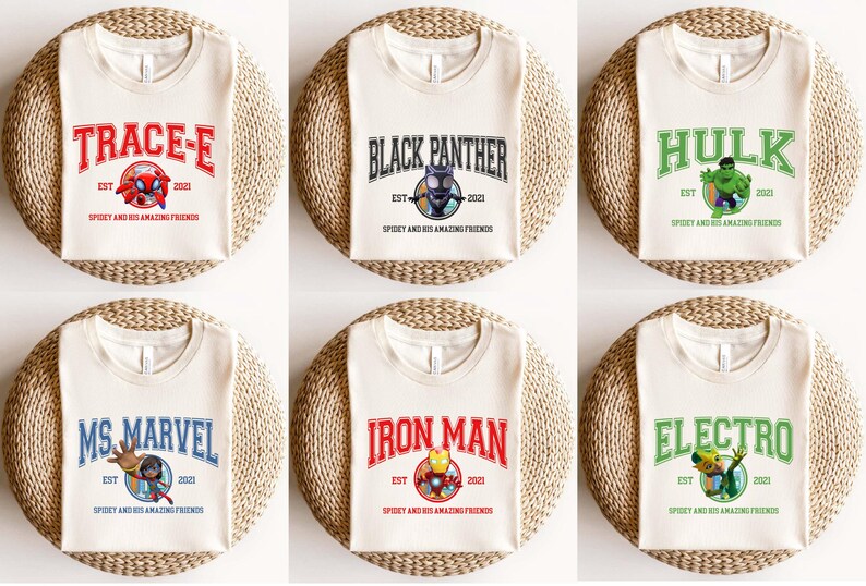May include: Six cream-colored t-shirts with different superhero character designs. Each shirt features a colorful graphic of a superhero, the superhero's name in a colorful banner, and the text "EST 2021 SPIDEY AND HIS AMAZING FRIENDS".
