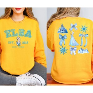 Elsa two sided bow sweatshirt and hoodie inspired by Frozen Disney princess style. Cozy unisex crewneck sweatshirt featuring front and back bow design aesthetic. Perfect Disney girls trip sweatshirt for Disneyland and Disney World vacations. Soft and comfortable Disney sweatshirt ideal for park outfits, travel days, or casual wear. Cute coquette Elsa sweatshirt great for girls, friends, and Disney fans.