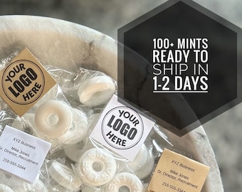 May include: A close-up of a white marble surface with multiple small, clear plastic bags containing white round mints. Each bag has a brown paper label with the text "YOUR LOGO HERE" and a business card with the text "XYZ Business, Mike Jones, Sr. Director, Recruitment, 216-555-3344". The text "100+ MINTS READY TO SHIP IN 1-2 DAYS" is printed in black on a white hexagonal background.