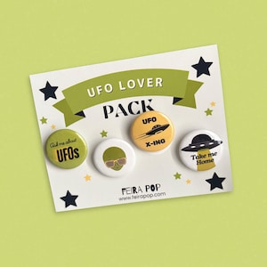 May include: A pack of four UFO-themed pinback buttons on a white card with a green banner that reads "UFO Lover Pack." The buttons feature alien and spaceship designs with text like "Ask me about UFOs" and "Take me Home."