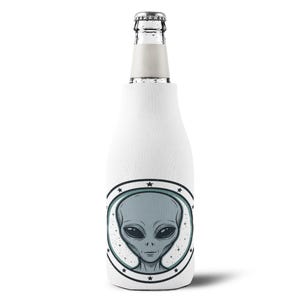 May include: White beer bottle cooler with a gray alien face design. The alien is inside a circular emblem with stars. The cooler is designed to keep beverages cold and is a fun accessory for any gathering.