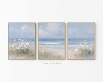 May include: Three framed art prints depicting a serene beach scene. Each print features a light blue sky, ocean waves, and white flowers in the foreground. The artwork is signed "Golden Fields Studios".