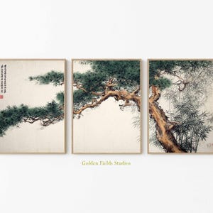 May include: A triptych of framed art prints displaying traditional Asian tree paintings. The artworks depict pine and bamboo trees with green foliage and brown trunks on a cream backdrop. The frames are light brown. The text "Golden Fields Studios" is visible.