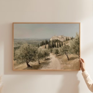 Puede incluir: Pintura de paisaje enmarcada que representa una escena de un pueblo toscano. La obra presenta olivos, un camino de tierra y un pueblo distante con edificios. La paleta de colores incluye verdes apagados, marrones y azules, creando una atmósfera serena.