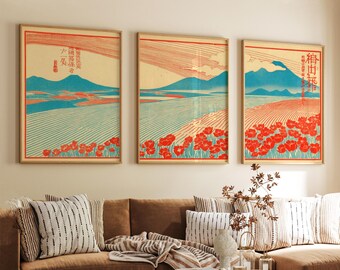 May include: Three framed art prints with a Japanese landscape theme. Each print features a mountain, field, and red flowers. The color palette includes blue, red, and beige. The prints are displayed above a brown sofa with decorative pillows.