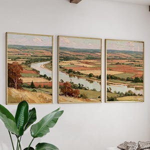 May include: A triptych of landscape paintings featuring a winding river flowing through a valley of golden, green, and reddish-brown fields under a pale sky. Each rectangular canvas is framed in a thin gold border, displaying textured brushstrokes.