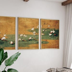 May include: Three framed wall art pieces with a vintage aesthetic. Each features a gold frame and a painting of white flowers on branches over a green and gold background. The artwork evokes a sense of traditional Asian art.