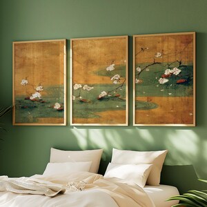 May include: Three framed art prints depicting a serene pond scene with white blossoms and red accents. The artwork features a gold background and a green pond with lily pads. The frames are gold, and the overall aesthetic is calming and nature-inspired.