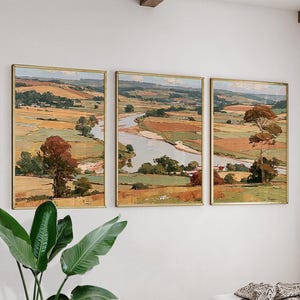 Könnte beinhalten: Ein Triptychon aus Landschaftsgemälden, das einen sich schlängelnden Fluss durch hügelige Landschaften, Felder in Ocker-, Grün- und Brauntönen sowie vereinzelte Bäume zeigt. Jede rechteckige Leinwand ist in einen dünnen Goldrahmen gefasst.