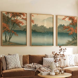 Könnte beinhalten: Ein Set aus drei rechteckigen Wandbildern, die eine Landschaft mit einem ruhigen blauen See, fernen Bergen und Bäumen mit leuchtend orangefarbenem Laub zeigen. Jeder Druck ist in einem dünnen, hellen Holzrahmen eingefasst und nebeneinander angeordnet.