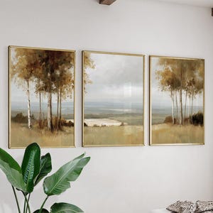 Könnte beinhalten: Set aus drei gerahmten Landschaftskunst-Drucken. Jeder Druck zeigt eine ruhige Szene von Bäumen und Feldern in gedämpften Tönen von Braun, Beige und Grün. Das Kunstwerk ist in goldfarbene Rahmen gefasst und schafft so eine zusammenhängende und elegante Darstellung.