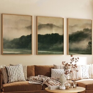 Puede incluir: Un tríptico de láminas de arte enmarcadas que muestra un paisaje forestal brumoso con árboles de color verde oscuro y colinas onduladas en tonos tierra apagados. Las tres piezas rectangulares se muestran una al lado de la otra.