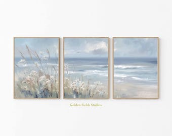 May include: Three framed wall art prints depicting a serene coastal scene. Each print features a soft, muted color palette of blues, whites, and beige, with a focus on the ocean, sky, and beach. The artwork includes delicate floral and grassy elements.