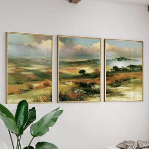 May include: A triptych of landscape paintings featuring rolling hills, fields in shades of green, brown, and gold, and a small house nestled in the distance under a cloudy, atmospheric sky. The artwork is displayed in three separate frames.