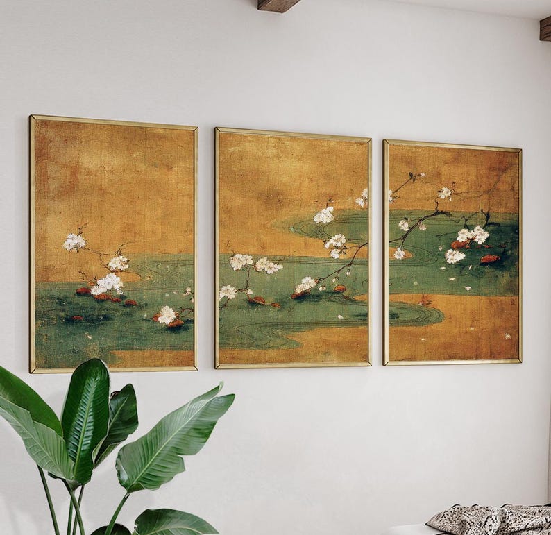 May include: Set of three framed art prints featuring a traditional Japanese painting style. Each print depicts a scene with white cherry blossoms, green water, and a golden background. The frames have a gold finish.