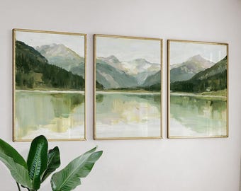 May include: A triptych of framed landscape paintings featuring mountain ranges and a calm lake in shades of sage green, olive, and soft white. Each rectangular piece is encased in a thin gold frame, depicting a serene natural vista.