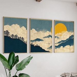 May include: A set of three framed art prints depicting a mountain landscape. Each print shows a blue sky, white clouds, and a golden sun. The artwork has a minimalist style, focusing on natural elements.