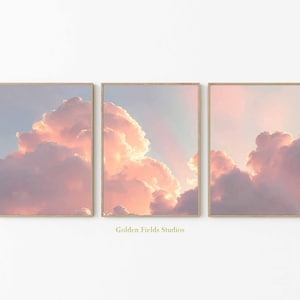 Pode incluir: Conjunto de três impressões emolduradas com nuvens rosa pastel e pêssego contra um céu azul claro. As obras de arte são exibidas em molduras de madeira. O texto "Golden Fields Studios" está na parte inferior.