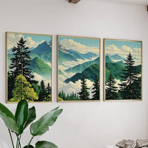 Könnte beinhalten: Dreiteiliges Set gerahmter Landschaftskunst-Drucke. Jeder Druck zeigt eine Berglandschaft mit grünen Bäumen, blauen Bergen und einem bewölkten Himmel. Die Rahmen haben eine goldene Oberfläche, die dem Kunstwerk Eleganz verleiht.